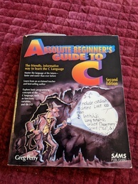 Absolute Beginner's Guide to C book cover. Features a man dressed similarly to Indiana Jones inside a cave shining a flashlight on some C code inscribed on the wall.