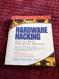 Hardware Hacking manual. Red strip at the top with a quote from Kevin Mitnick, appears to have a picture of nearly unrecognizable hardware which has been cut away revealing the title underneath. Lists a lot of quotes and a lot of authors that apparently contributed